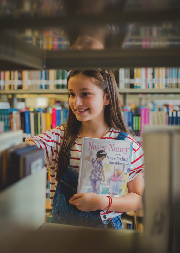 A girl holding up an english book in front of some books.